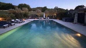 Una piscina rettangolare con sedie a sdraio e un muro in pietra su un lato.