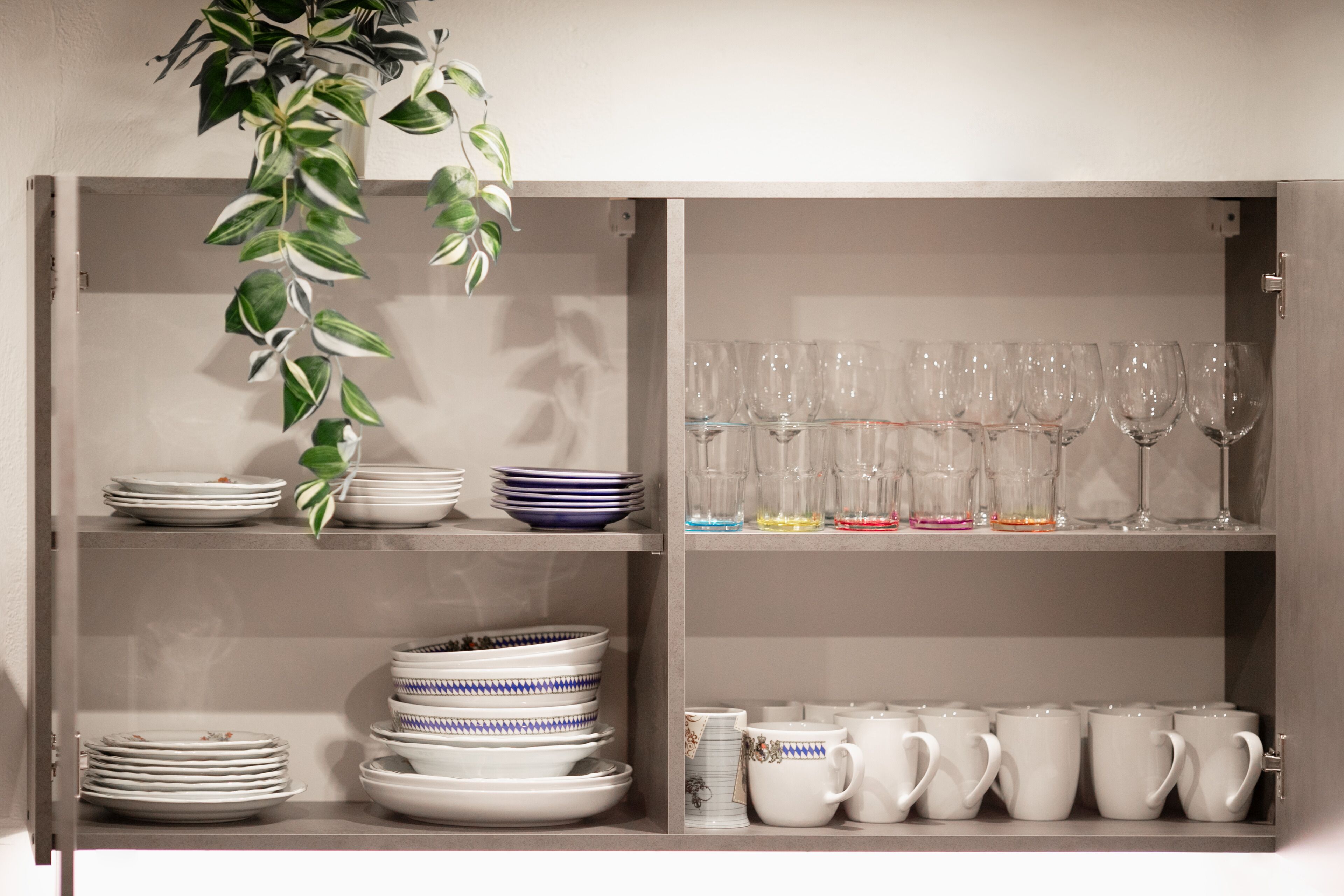 A kitchen cabinet with shelves holding plates, bowls, and cups.