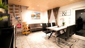 Un espace repas moderne avec une table blanche, des chaises noires, un canapé gris et un tableau représentant un paysage.