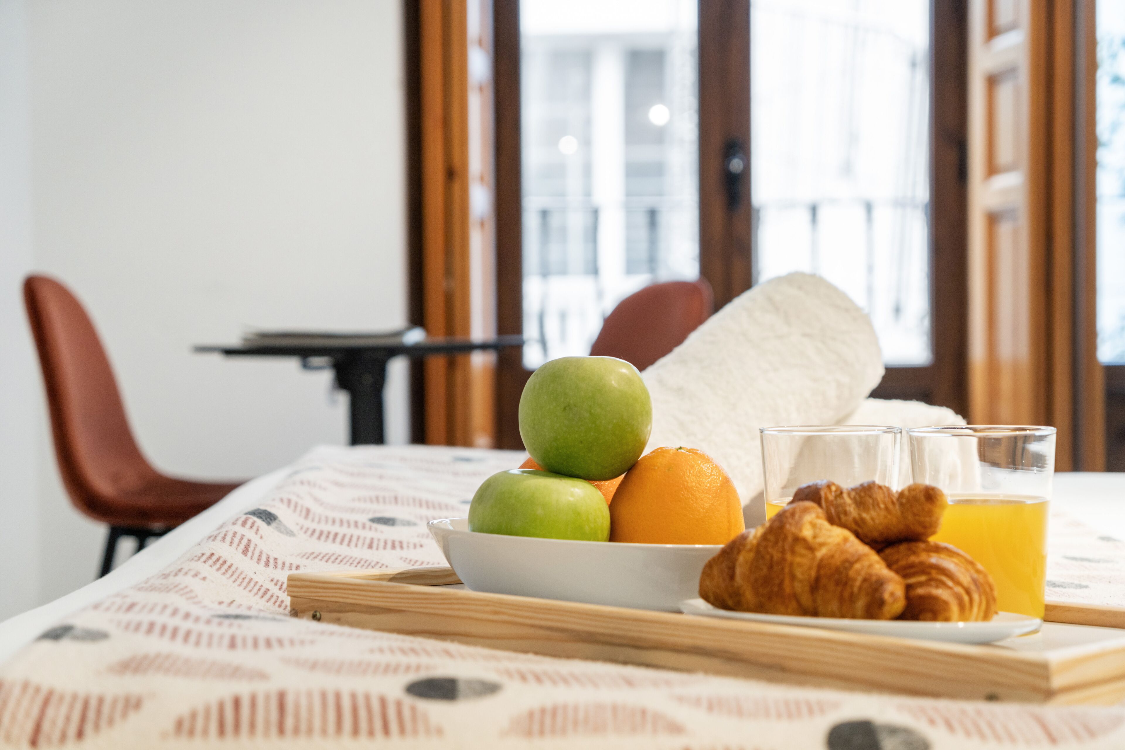 Un desayuno con un bol de fruta, croissants y zumo de naranja sobre una mesa.