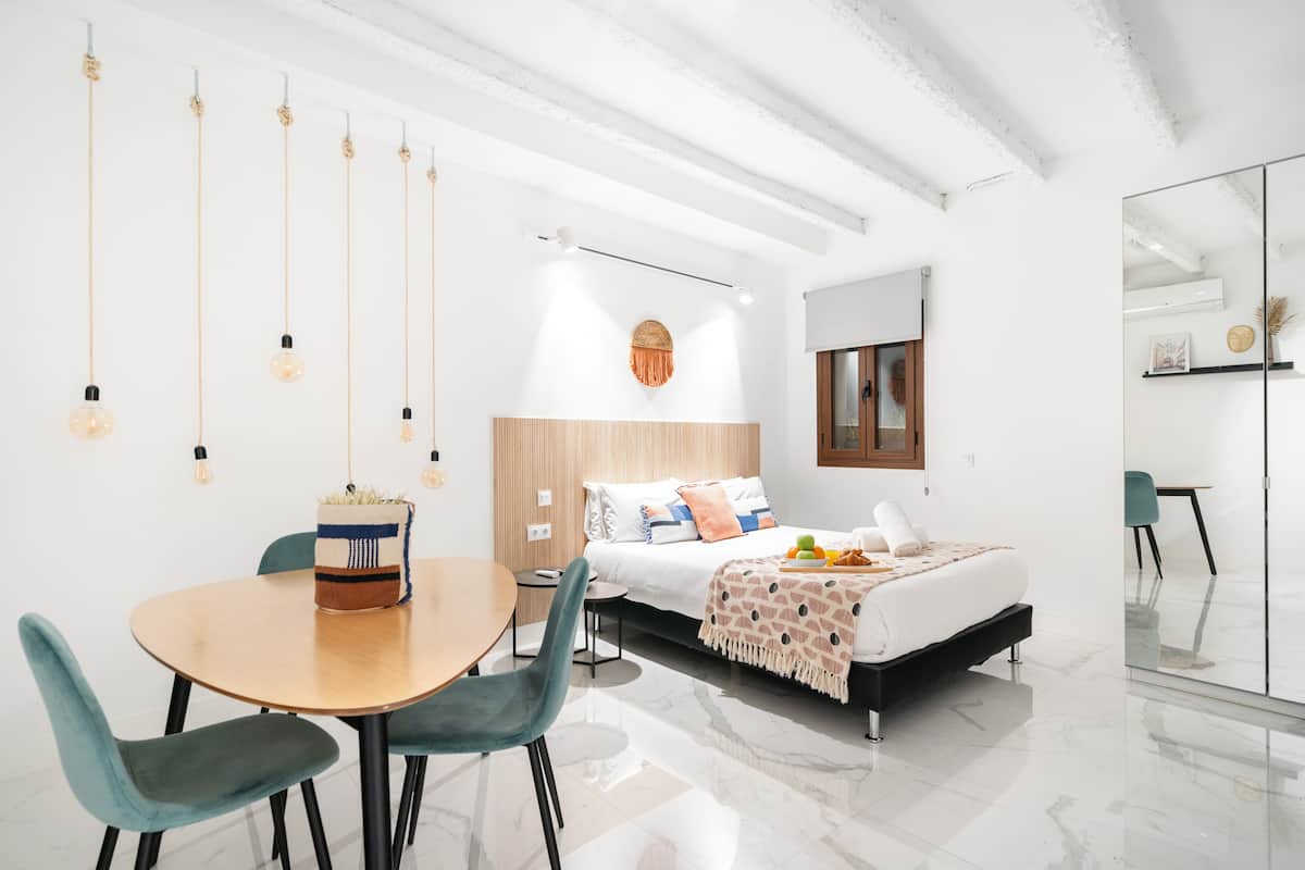 A modern bedroom with a bed, bedside table, and a dining area with chairs.