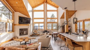 Un salón amplio con chimenea, ventanas grandes y una cocina con barra.