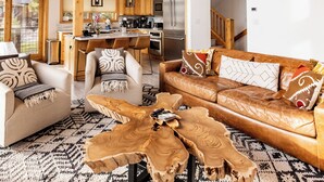 Un salón amplio con techo alto, vigas de madera, una mesa de centro y un sofá con cojines estampados.