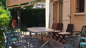 Een buitenterras met een tafel en stoelen, een gestreepte luifel en een gebouw op de achtergrond.