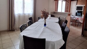 Een eethoek met een ronde tafel, stoelen en een vaas met gedroogde bloemen.