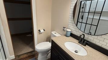 A bathroom with a toilet, sink, mirror, and a shower area.