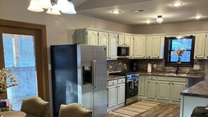 A modern kitchen with white cabinets, stainless steel appliances, and a dining area with a wooden table and chairs. - Cowtown at Piney River Ranch; Charming Farm House in Houston, MO (Houston)