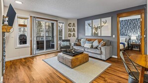 A spacious living room with a grey sofa, a wooden coffee table, and a fireplace. - Welcoming 2 Bed/2 Ba-View-Pet-Gym-Parking-Wash/Dry (Canmore)