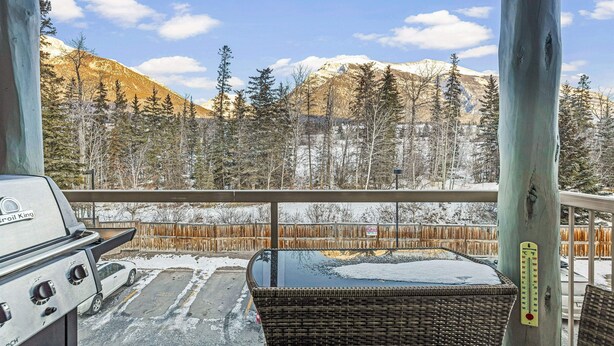A balcony with a view of snow-covered mountains, a wicker chair, and a grill. - Welcoming 2 Bed/2 Ba-View-Pet-Gym-Parking-Wash/Dry (Canmore)