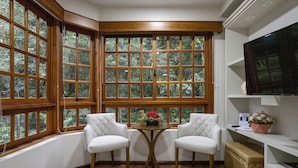 Ein Eckzimmer mit zwei weißen Polsterstühlen, einem kleinen runden Tisch mit einer roten Blumenvase und einem großen Fenster mit vielen Fensterscheiben.
