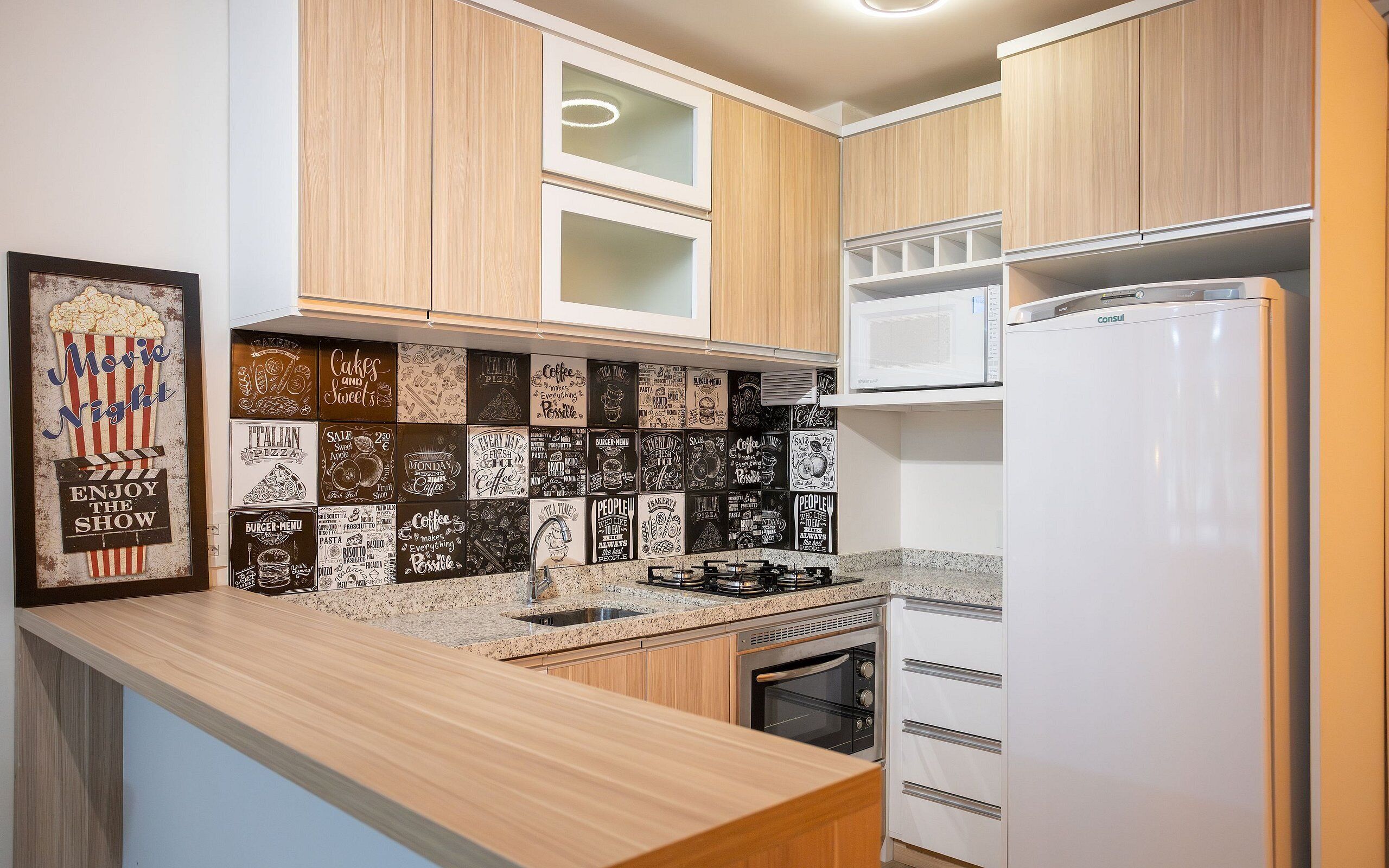 A modern kitchen with wooden cabinets, a white refrigerator, a microwave, a gas stove, and a tiled backsplash with various food-related designs.