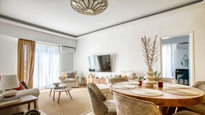Un salon moderne avec un coin repas, comprenant une table ronde en bois, des sièges confortables et un téléviseur à écran plat fixé au mur.