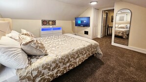 Un dormitori amb llit, televisió, prestatge i mirall.