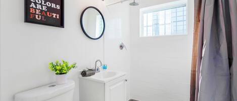A bathroom with a toilet, sink, mirror, shower, and a motivational quote on the wall.