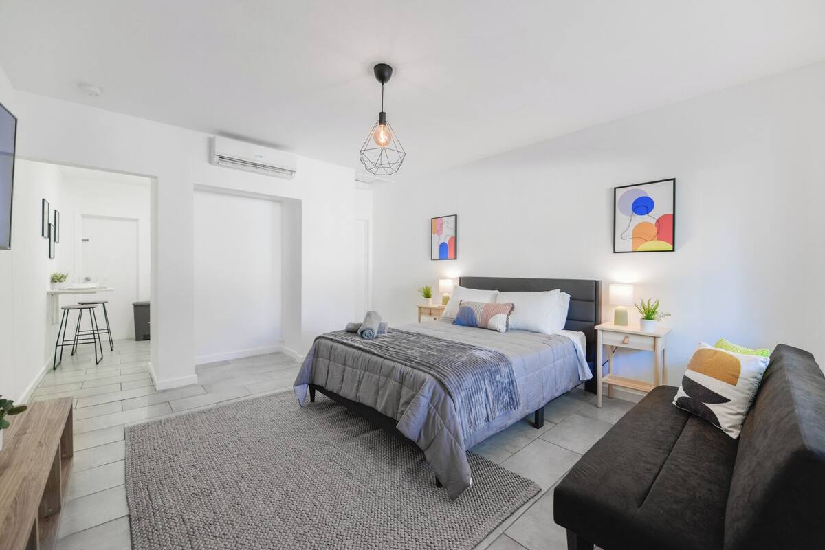 A modern bedroom with a bed, bedside tables, a desk, and a sofa.