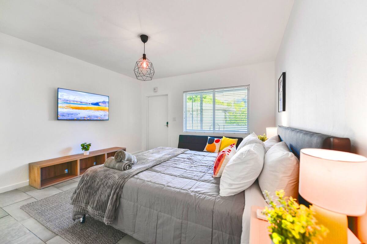 A modern bedroom with a bed, bedside table, lamp, and a painting on the wall.