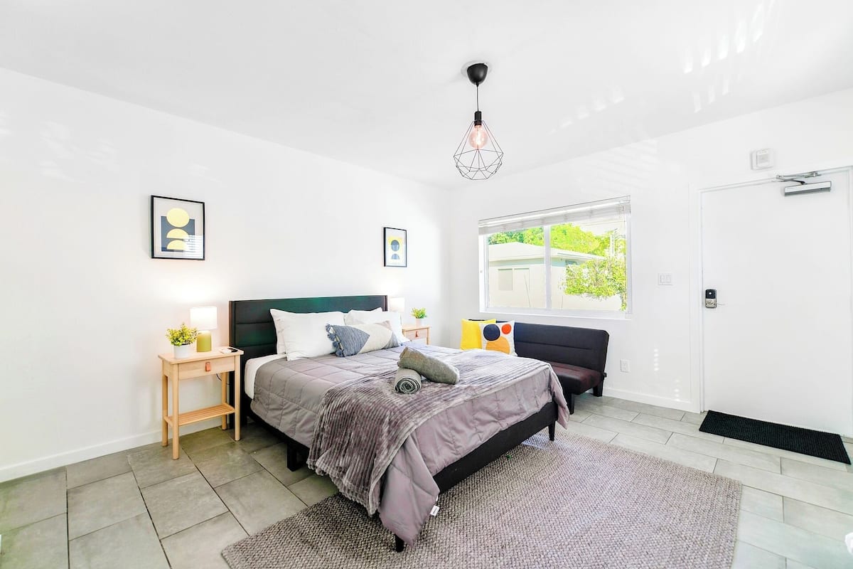 A modern bedroom with a bed, bedside tables, a window, and a unique geometric pendant light.