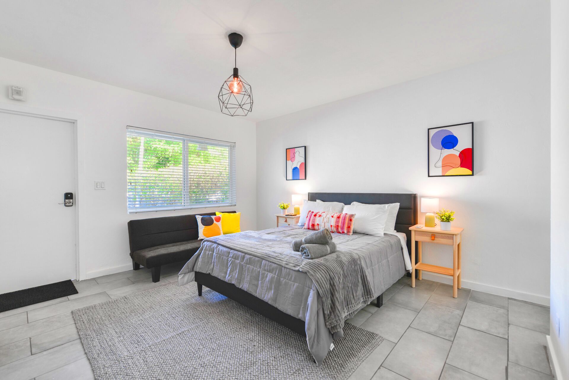 Een moderne slaapkamer met een bed, nachtkastjes, een bankje en kunstwerken.