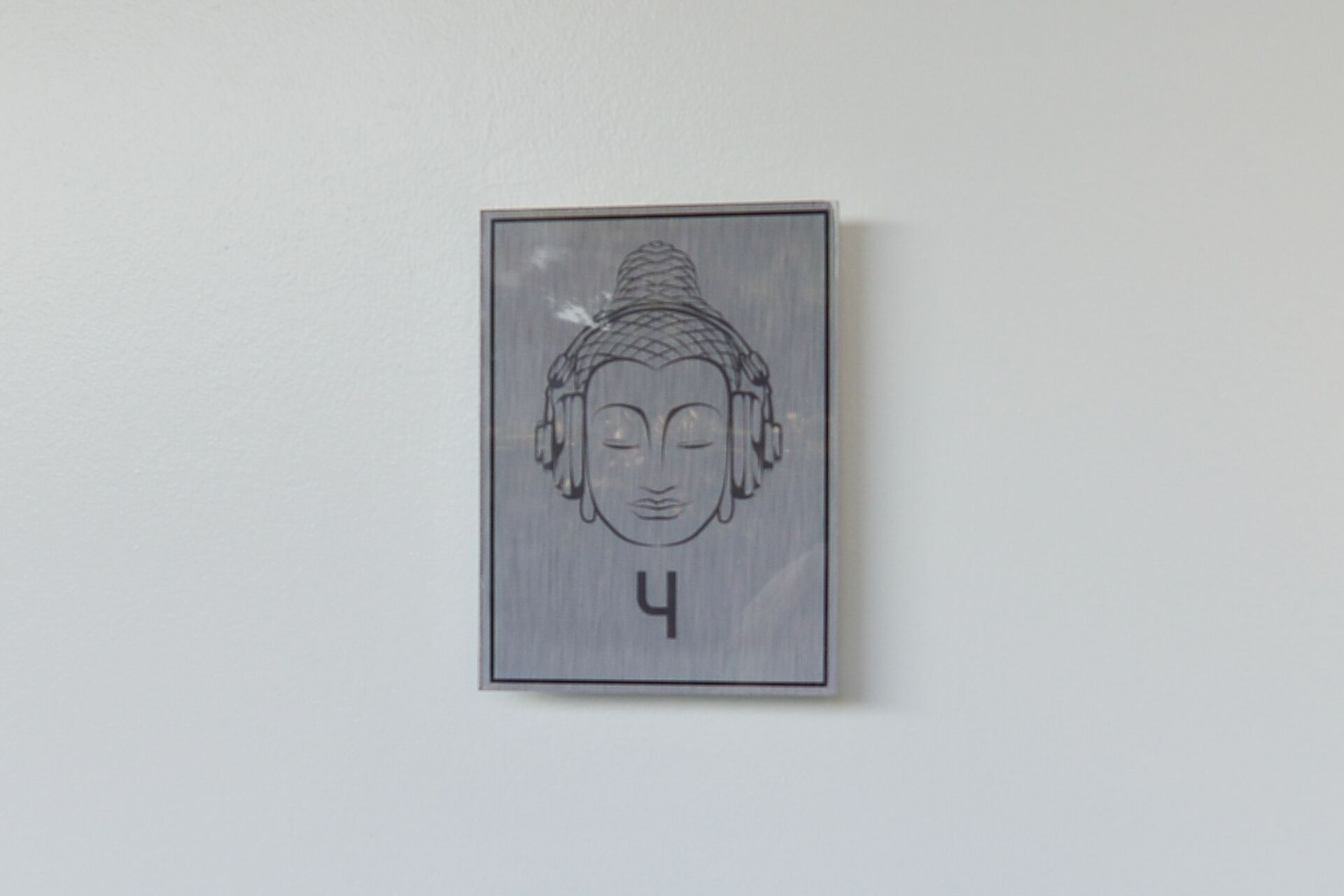 Una obra de arte colgada en la pared, representando la cabeza de Buda con una expresión serena, enmarcada en un borde rectangular sencillo.
