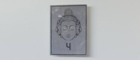 Una obra de arte colgada en la pared, representando la cabeza de Buda con una expresión serena, enmarcada en un borde rectangular sencillo.