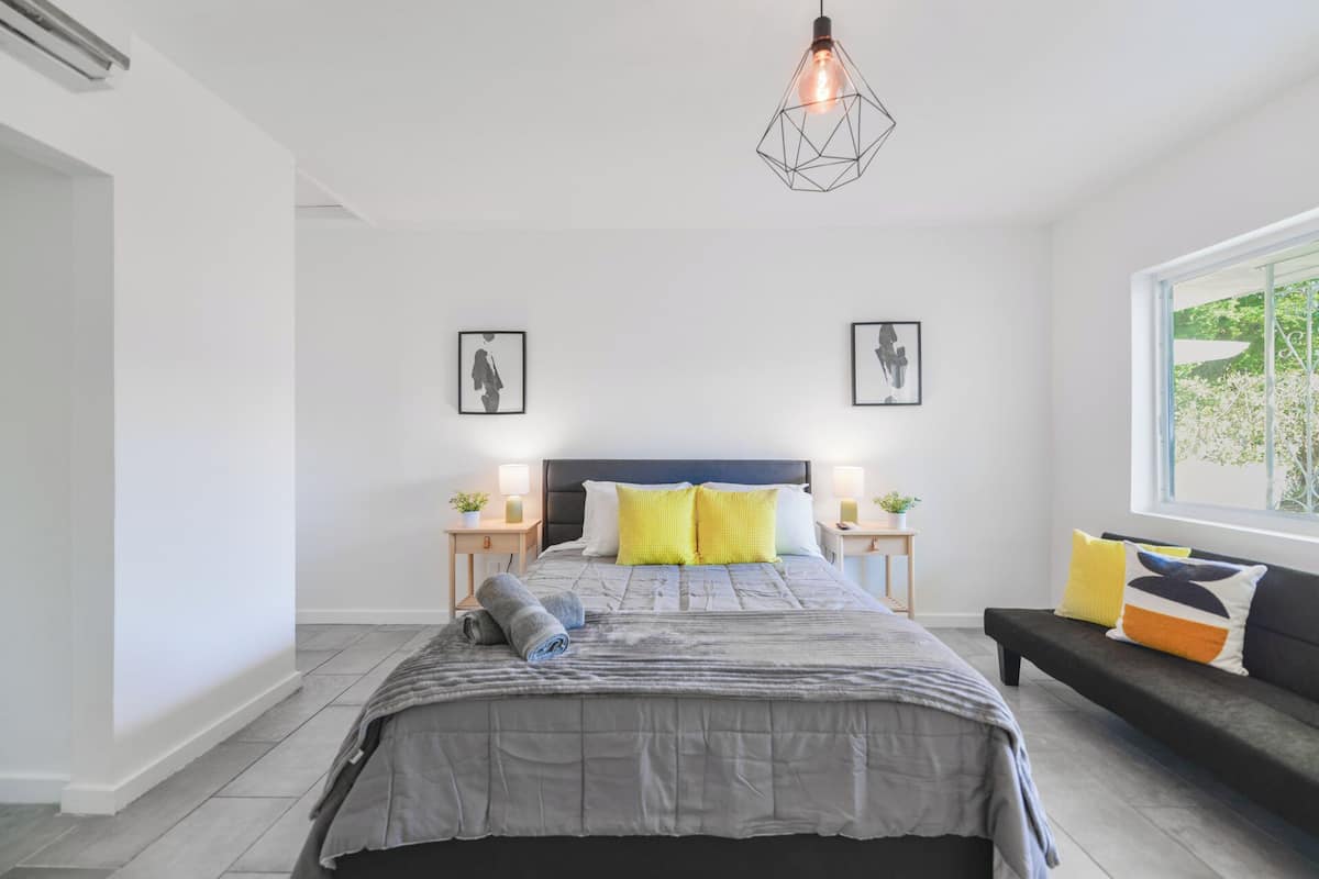 A modern bedroom with a bed, bedside tables, a nightstand, a sofa, and a window with a view.