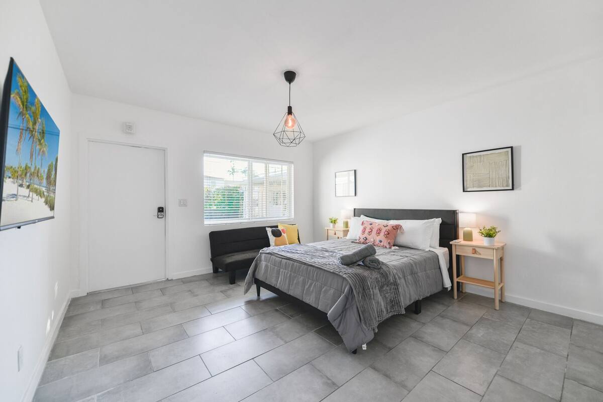 A bedroom with a bed, bedside tables, a window, and a painting on the wall.