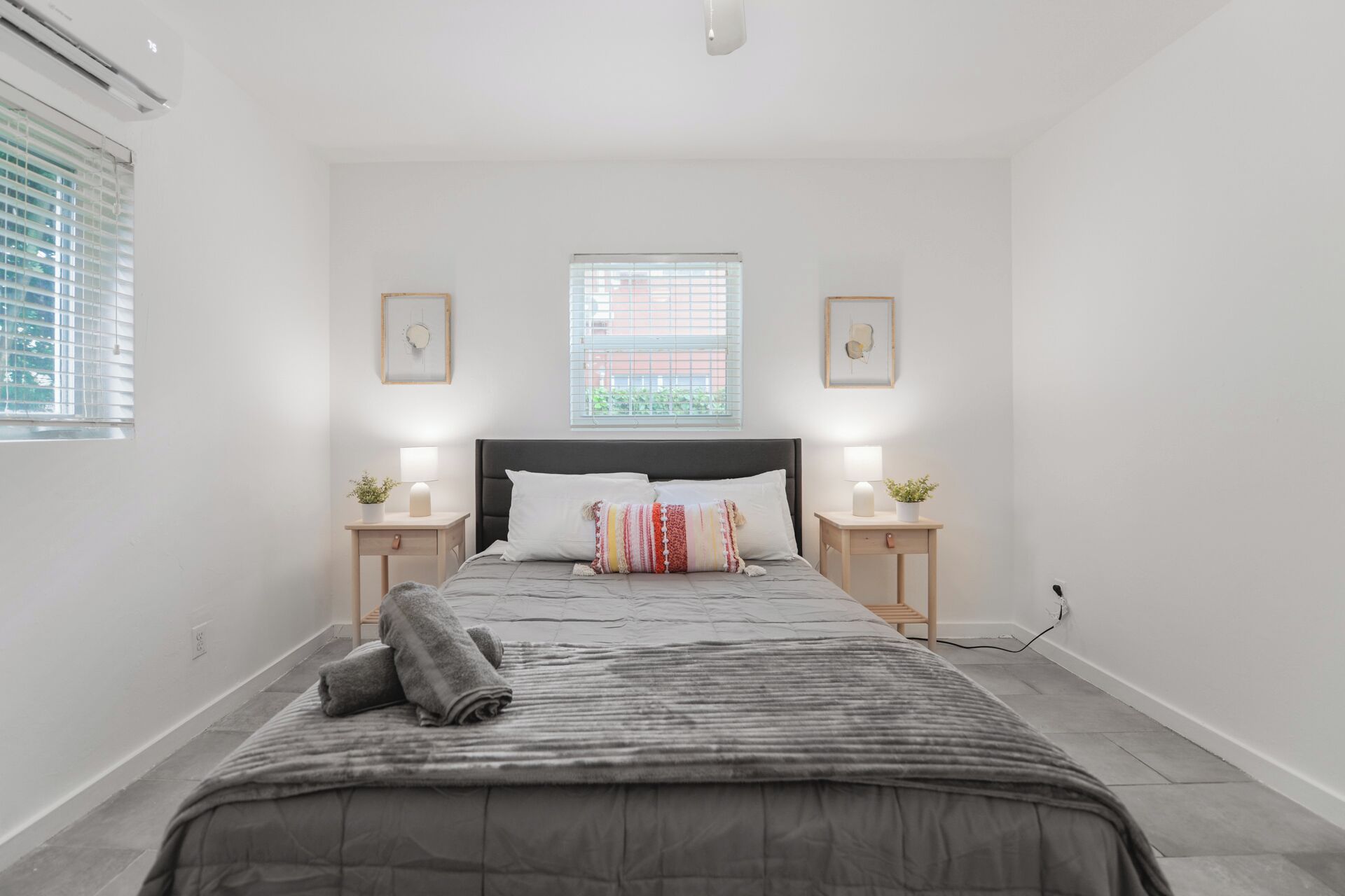 Un dormitorio con una cama, dos mesitas de noche, un ventanal y un aire acondicionado instalado en la pared.