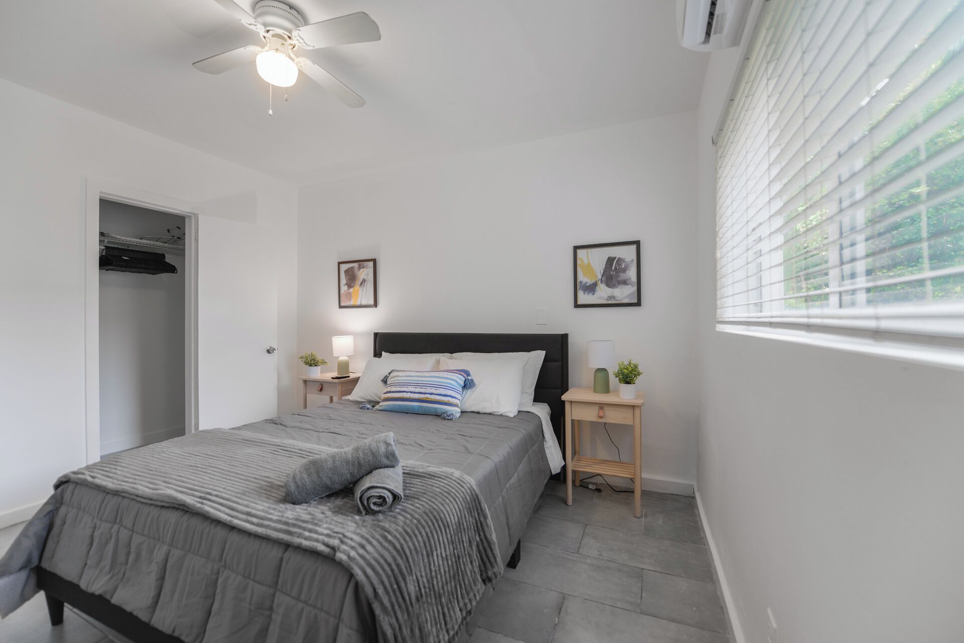 A bedroom with a bed, bedside tables, a ceiling fan, and a window with blinds.