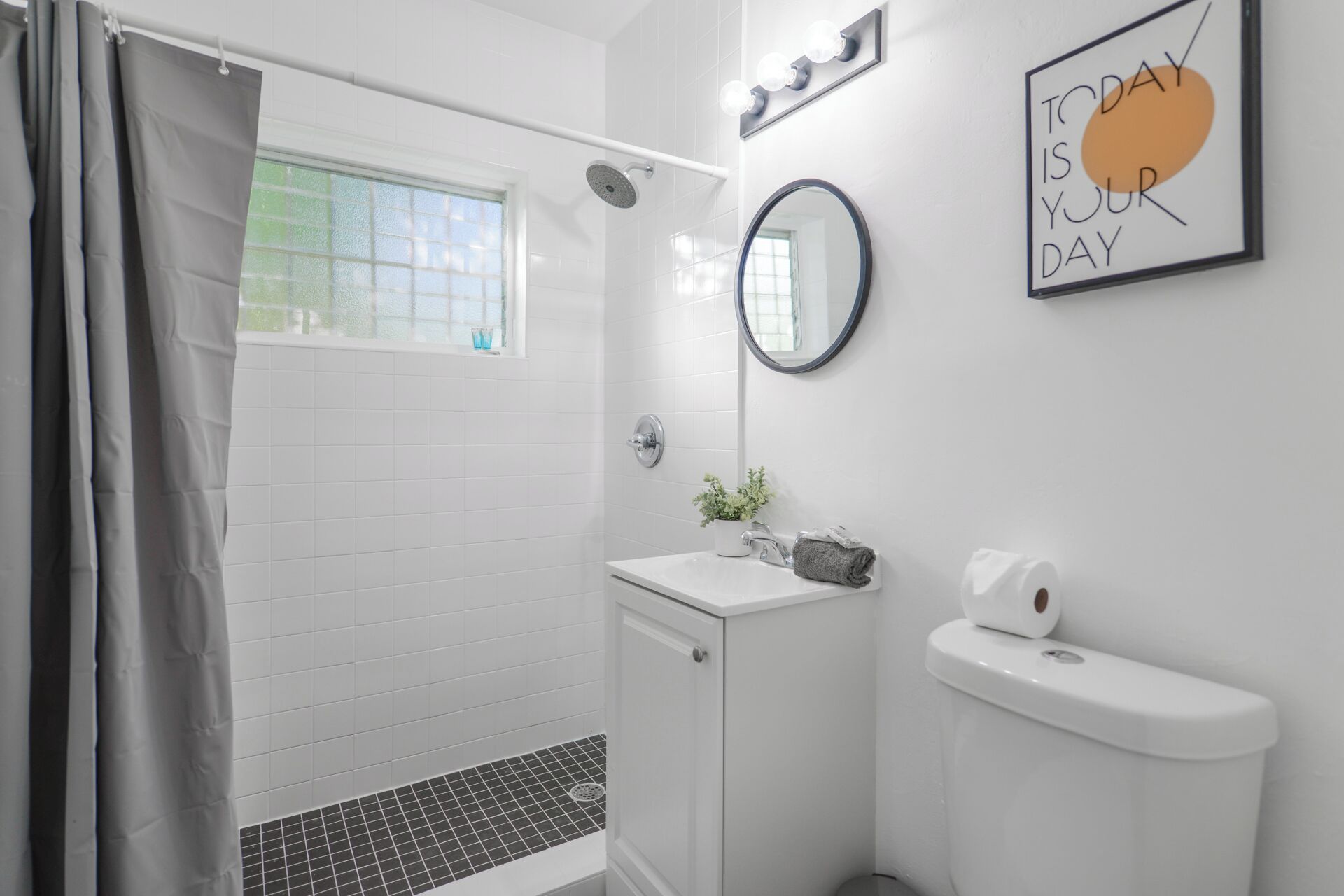 A modern bathroom with a shower, toilet, and sink. There is a window with a view, a mirror, and a motivational quote on the wall.