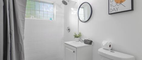 A modern bathroom with a shower, toilet, and sink. There is a window with a view, a mirror, and a motivational quote on the wall.