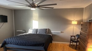 A bedroom with a bed, a ceiling fan, a nightstand, a dresser, and a wall-mounted TV. - The Shack- 3 bedroom finished house (Leadwood)