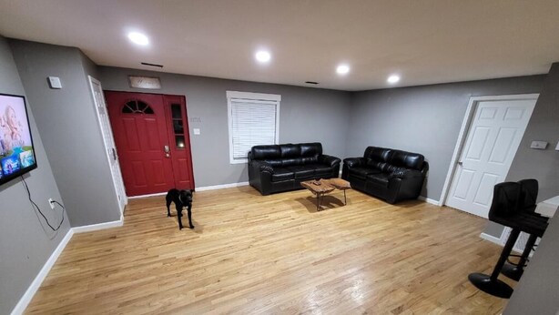A living room with hardwood flooring, two black leather sofas, a coffee table, and a TV mounted on the wall. - The Shack- 3 bedroom finished house (Leadwood)