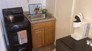 A compact kitchen with wooden cabinets, a stainless steel sink, a kettle on the stove, and a coffee machine.