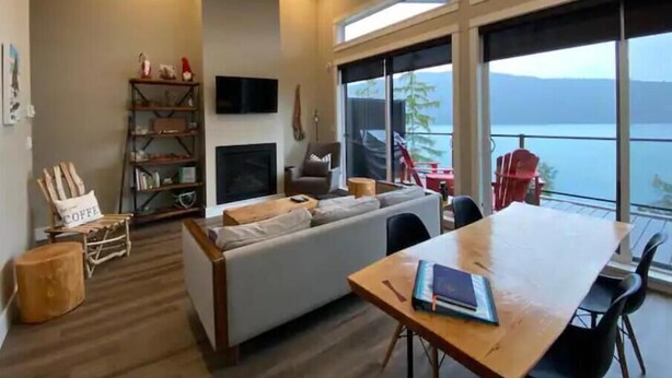 Een moderne woonkamer met een bank, salontafel, televisie en een groot raam met uitzicht op water.