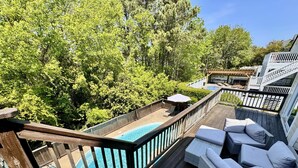 Une terrasse en bois avec une piscine, des meubles en osier et une vue sur les arbres.