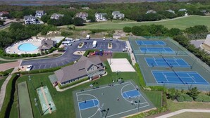 Vue aérienne d’un complexe sportif comprenant plusieurs courts de tennis, une piscine et un parking.
