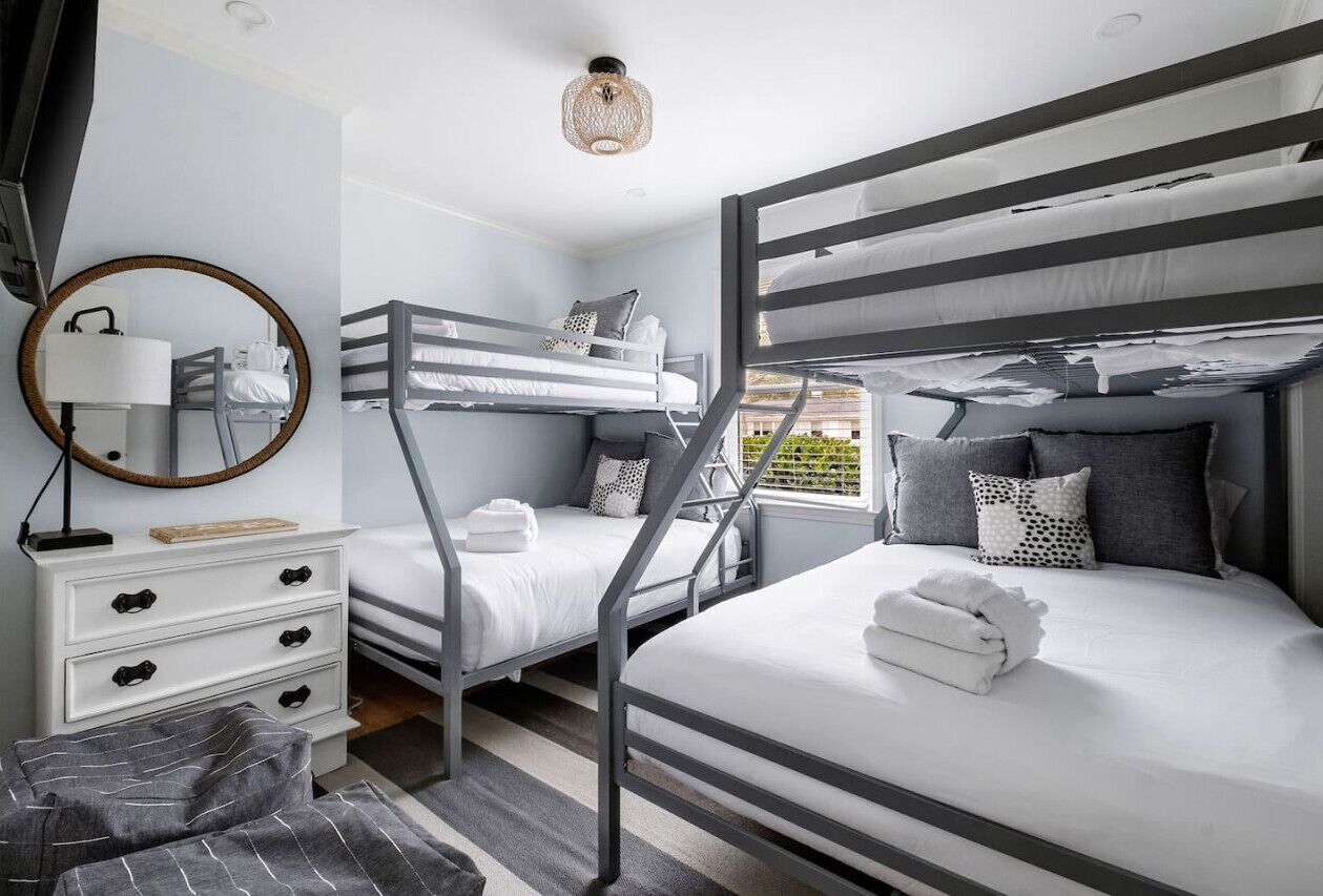 Een moderne, compacte kamer met stapelbedden, een witte dressoir met lades, een ronde spiegel en een klein vloerkleed.