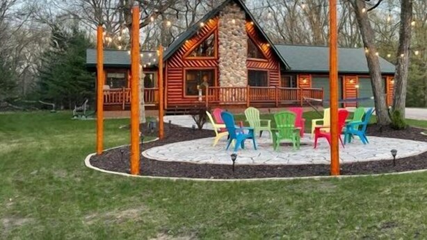 A lodge with a stone exterior, a porch with wooden railings, and colorful plastic chairs arranged in a circle. - Stunning Lake Petenwell Log Home Near Sand Valley Golf (Rome)