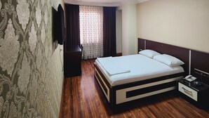 Une chambre d’hôtel avec un grand lit, une table de chevet avec une lampe, un téléviseur fixé au mur et un papier peint à motifs.