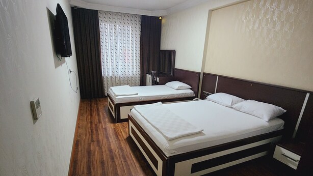 Une chambre d’hôtel avec deux lits, un plancher en bois, un téléviseur à écran plat fixé au mur et une fenêtre avec des rideaux.