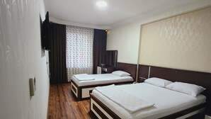 Une chambre d’hôtel avec deux lits, un plancher en bois, un téléviseur à écran plat fixé au mur et un luminaire au plafond.