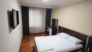 Une chambre d’hôtel avec un plancher en bois, un lit avec une literie blanche, un téléviseur à écran plat fixé au mur et une fenêtre avec des rideaux.