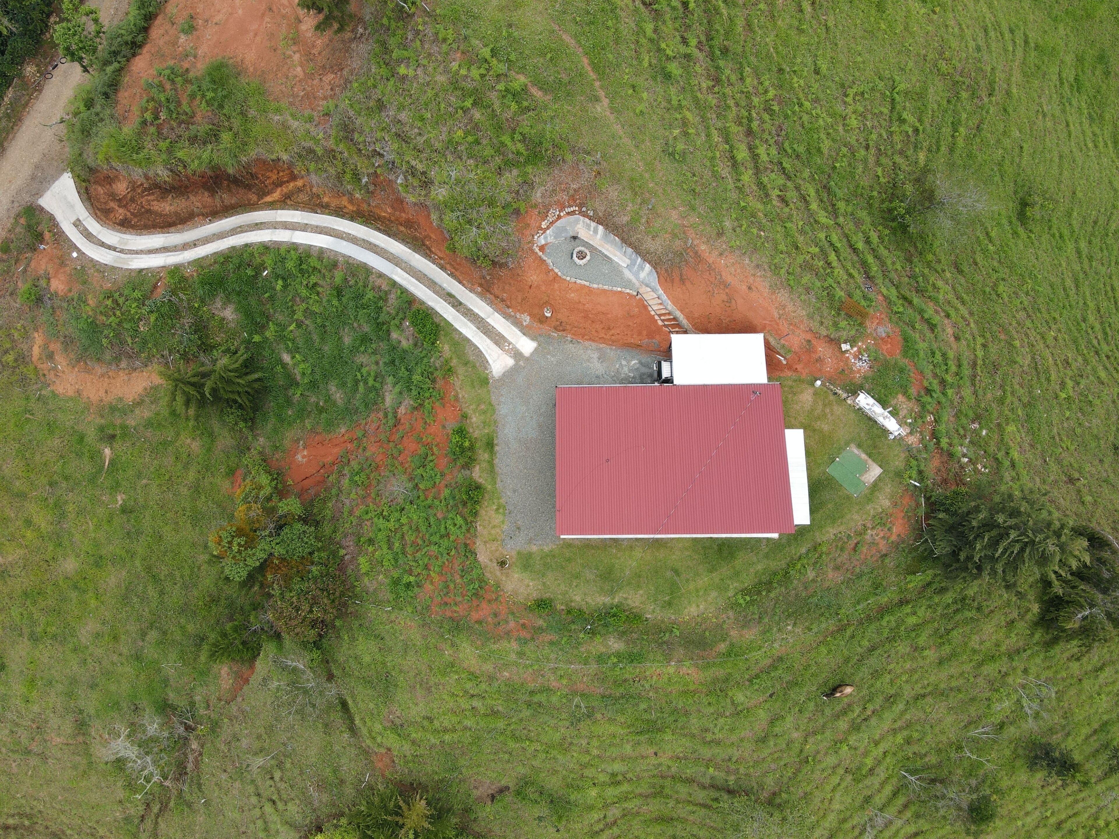 Vista aérea de una propiedad con un edificio de techo rojo, un camino sinuoso y una pequeña estructura blanca.