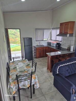 Una cocina compacta con refrigerador, microondas y cafetera. Hay una mesa de comedor con sillas y un sofá.