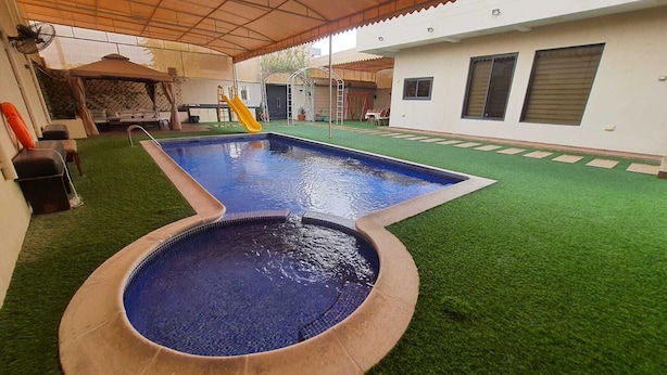 A swimming pool with a slide, surrounded by artificial grass and a covered area with a fan. - Charming 2-bedroom villa with Swimming pool, WiFi and AC in enchanting Shahrakan (Shahrakan)