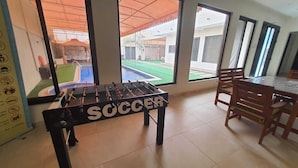 A foosball table labeled "SOCCER" in a room with large windows, a dining area with wooden chairs, and a tiled floor. - Charming 2-bedroom villa with Swimming pool, WiFi and AC in enchanting Shahrakan (Shahrakan)