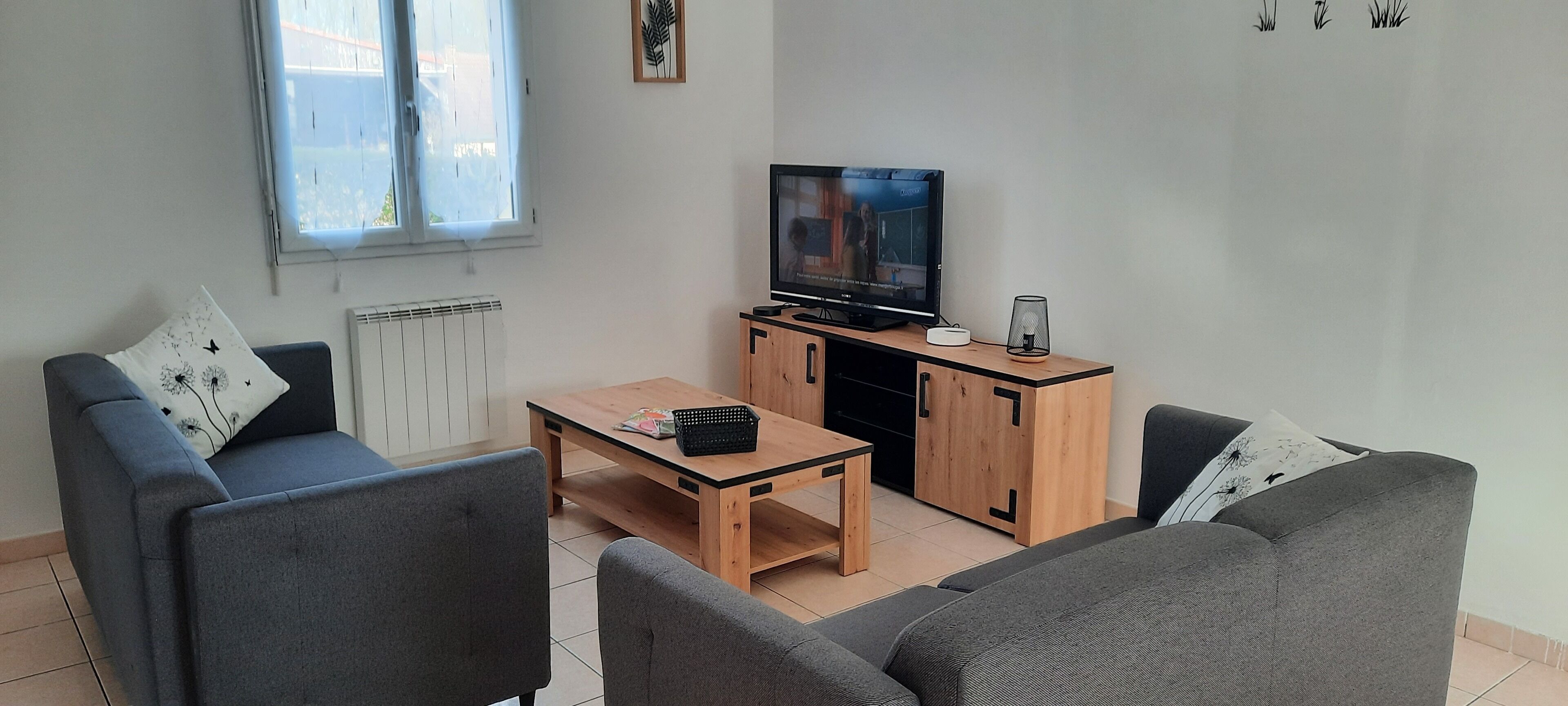 Ein modernes Wohnzimmer mit einer Sofagarnitur, einem Couchtisch, einem Fernseher auf einem Holzschrank und einer Heizung.