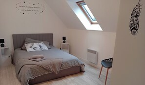 Une chambre à coucher moderne avec un puits de lumière, un lit recouvert d’une courtepointe à carreaux, des tables de chevet avec des lampes et un radiateur.