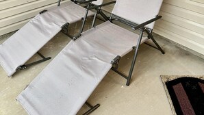 En uppsättning bestående av tre loungestolar med metallram och grå tygklädsel, placerade på en betongterrass intill ett beige hus med vita fönsterluckor.