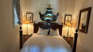 A neatly made bed with white linens, flanked by two bedside tables with lamps, a large decorative vase above the headboard, and framed pictures on the walls.